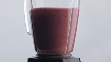 Lezzetli vitamin kokteylleri karıştırıcı süper yavaş çekimde harmanlanıyor. Lezzetli meyve suyu karışımı elektrikli blender kabının beyaz arka planında. İyileşmek için antioksidan smoothie hazırlanıyor..