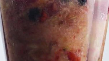 Kapanış rotasyonu blender cam kasenin içindeki meyveleri çok yavaş çekimde harmanlıyor. Meyveli, çilekli, meyveli, çilekli, portakallı, tatlı suyla karıştırılmış meyve suyu..