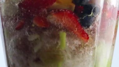 Cam blender kasesinin içinde taze meyve meyveleri dönüyor. Hem de çok yavaş çekimde. Lezzetli yaban mersinli, portakallı elmayla elektrikli mikserde temiz su karışımı. Sağlıklı meyve suyu pişir..