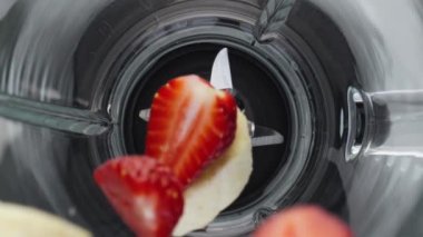 Kapalı taze dilimlenmiş blender kasesi süper yavaş çekimde düştü. Çelik bıçaklarla cam karıştırıcıya düşen olgun çilekli muz aromalı nar. Sağlıklı beslenme kavramı.