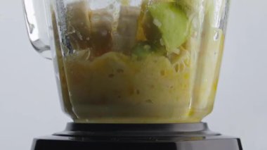 Elektrikli blender çok yavaş çekimde lezzetli vitamin meyvesi karışımı hazırlıyor. Cam karıştırıcı beyaz arka planda sulu taze muz portakalı karışımı. Vejetaryen sağlıklı yiyecekler pişirmek.