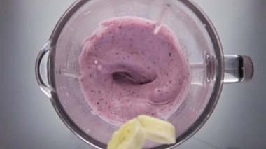 Dilimlenmiş tatlı muz blender kasesinde kıvrılarak meyveli içeceğe düşüyor. Üst görünüm organik meyve serpme vitamin sulu kokteyli süper yavaş çekimde düştü. İçmek için doğal malzemeler..