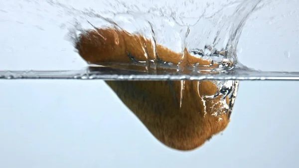 Pear splashed fizzy water closeup. Fresh yellow fruit fall under liquid with air bubbles. Establishing white background. Rural homegrown seasonal antioxidant inside glass. Raw nutrition concept