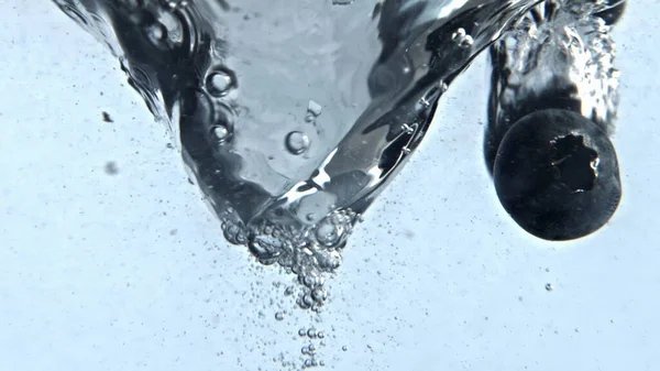 Detox liquid berries swirling clean vessel closeup. Clear aqua moving transparent glass in slow motion. Water with blueberries vortex with air bubbles white background. Ice carbonated cocktail funnel