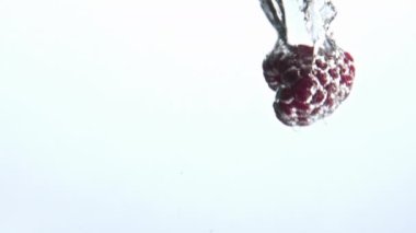 Pembe ahududu şelalesi su damlatıyordu. Makroda organik böğürtlen ile köpüklü berrak su. Şeffaf sıvı akvaryuma atılan tatlı kırmızı yemek beyaz arka plan. Yaz konsepti 