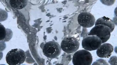Meyve suyu köpüklü suyun içinde hareket ediyor. Şeffaf bir bardak maden suyunda dönen büyük yaban mersinleri. Soğuk sıvı kadehte ağır çekimde dönen lezzetli doğal tatlı. Organik gıda konsepti