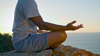 Akşam vakti okyanus ışığında Lotus pozisyonunu rahatlatan adam. Bilinmeyen Yogi, kayalık deniz kenarında meditasyon yapıyor. Zen insanının konsantre olması doğayla huzurlu bir bağın keyfini çıkarır. Sahildeki kaygısız uyum havası.