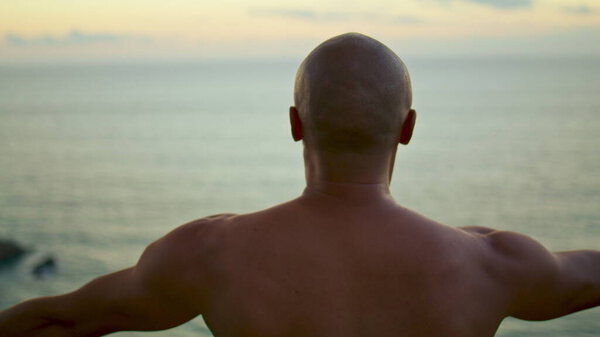Athlete practicing yoga spiritual exercise in beautiful ocean morning closeup. Unrecognized muscular bald man training concentrating topless outdoors. Zen like lifestyle. Inner harmony balance concept