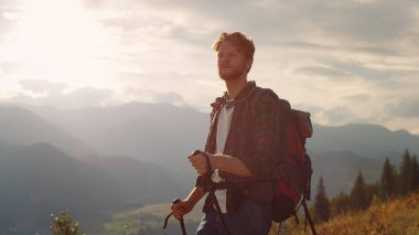 Closeup energetic hiker walk nature on mountains landscape. Hipster using trekking poles on tourism activity. Active backpacker enjoy look serene view on vacation. Wanderlust youth leisure concept.