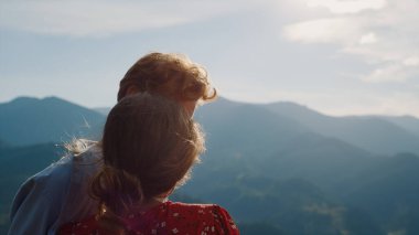 Eğlenceli çift dağ manzarasını sever. Doğa tatilinde mutlu aşıklar kucaklaşır. Arkaya bakan koca karısı güneşli bir günde çok güzel görünüyor. Yaz tatili balayı aşkı konsepti.