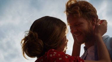 Yakınlaşan sevgi dolu çift dışarıda birbirine sarılıyor. Genç aşıklar güneşli, bulutlu gökyüzünün tadını çıkarırlar. Siluetler, sevgililer yaz tatilinde saçlarını okşar. Balayı aşk evliliği konsepti.