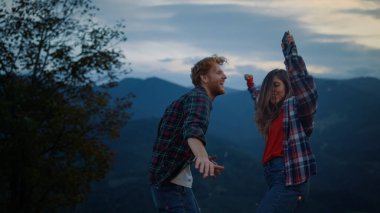 Joyful friends dance party in nature mountains landscape. Close up cheerful family enjoy fun travel on evening sunset. Happy tourists couple jump outside at dusk. Fun leisure active lifestyle concept.