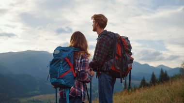 Close up two backpackers look sunrise mountains landscape. Hiking couple relax outside. Happy girlfriend boyfriend spend lovely date on active leisure. Young tourists on trekking. Travel concept.