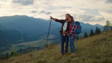 İki turist yaz yürüyüşünde dışarıda konuşuyor. Gülümseyen gezginler doğa yürüyüşü yapıyor. Yeşil Orman Tepesi manzarasını keşfeden mutlu bir çift. Spor gezginleri tatilin tadını çıkarır. Seyahat kavramı.