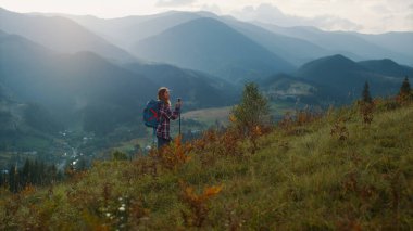 Active millennial travel mountains nature. Young woman trekking on landscape summer morning. Sporty explore walk on outdoors vacation. Excited tourist reach peak on green hill. Youth adventure concept