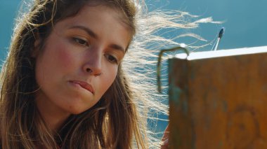 Doğada resim çizen yetenekli bir ressam. Rüzgarlı bir günde resim çizen yaratıcı kız portresi. Düşünceli ressam resim sehpası arıyor. Mükemmel renkleri yakına çekiyor. Sanat yaratma kavramı