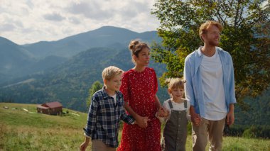 Active family enjoying travel on beautiful summer nature walking green mountain hill. Positive parents pointing fingers at amazing views outdoors. Relaxed couple spending time with happy children.