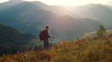 Active man walk mountains landscape. Sporty tourist hiking using trekking poles in morning sunrise. Backpacking hipster enjoy wanderlust travel lifestyle. Summer holiday activity recreation concept.