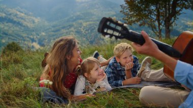 Unknown man playing guitar on picnic for wife kids close up. Happy family relaxing together listening music on green hill. Father hand holding fingerboard stringed instrument on summer holiday outdoor