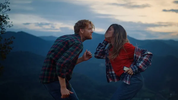 Dancing couple have fun in mountains evening. Happy lovers enjoy sunset active outdoors close up. Joyful girlfriend boyfriend move body by campfire party. Tourism holiday recreation happiness concept.