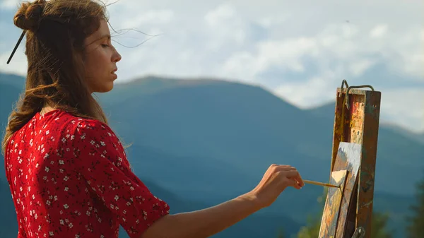 Closeup woman painter making brush stroke in summer mountains. Talented girl painting easel on nature view. professional artist drawing from nature outside. Young inspiring lady creating craft art
