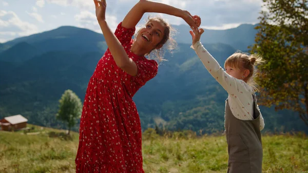 Happy mother with daughter spinning in dance summer holiday close up. Joyful woman dancing with cute girl on green meadow sunny day. Cheerful mom having fun with child jumping on grass outdoors.