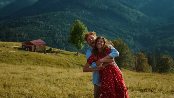 Young family dance together in summer mountains. Smiling couple have fun outside on sunny day. Laughing lovers embrace on holiday travel. Joyful husband wife relax on tourism activity. Love concept.