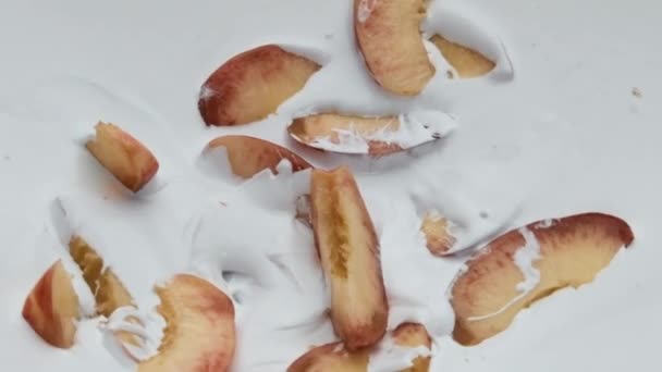 成熟的桃片躺在乳白色酸奶上 动作非常缓慢 美味多汁的水果掉进了乳酪甜点的背景中 素食营养的有机天然水果奶昔 — 图库视频影像