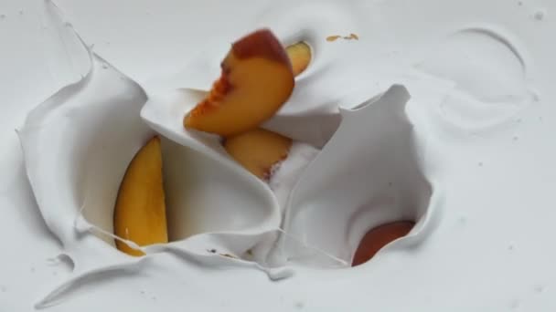 甘い桃の背景が熟した部分を持つ白い天然ヨーグルトが閉じます 超スローモーションでクリーミーな乳製品デザートに落ちるジューシーな甘いフルーツ 健康的なビタミンミルクシェイクのための有機ビタミン成分 — ストック動画