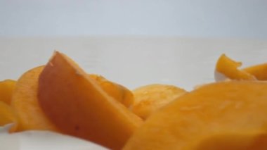 Lezzetli meyve arkaplanlı taze kayısı yoğurdu. Beyaz kremalı tatlı üzerinde uzanan parlak sarı dilimler süper yavaş çekimde. Lezzetli meyveli süt kahvaltısı. Sağlıklı yaşam tarzı kavramı.