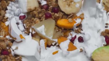 Tatlı tahıl gevreğine dökülen doğal yoğurt. Lezzetli meyveler. Çok yavaş çekimde. Pişmiş mısır gevreği, ananaslı kayısı, nar ve taze süt. Sağlıklı yemek.