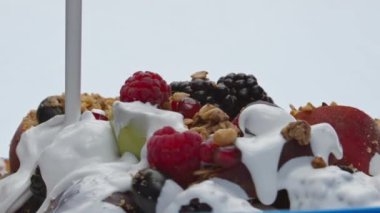 Lezzetli müsli, süper yavaş çekimde doğal Yunan yoğurdu döktü. Pişmiş tahıl ve tatlı meyve meyveleriyle akan taze süt sıvısı. Kahvaltı için ev yapımı vitamin yemeği hazırlıyorum..