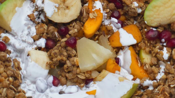 Sweet sliced fruits with cereals poured with fresh organic milk close up. Vitamin nutrient muesli with juicy pineapple apricot banana pomegranate apple preparing with white yogurt. Healthy food.