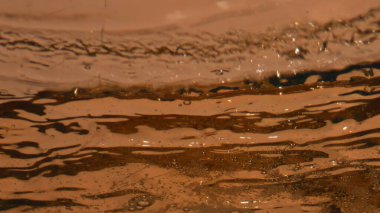 Karbonatlı bira sıçratma kadehi yakın plan. Şeffaf cam eşyanın içinde sıvı akıyor. Altın alkollü içecek, ağır çekimde sallanıyor. Sarhoş edici içecek konsepti 