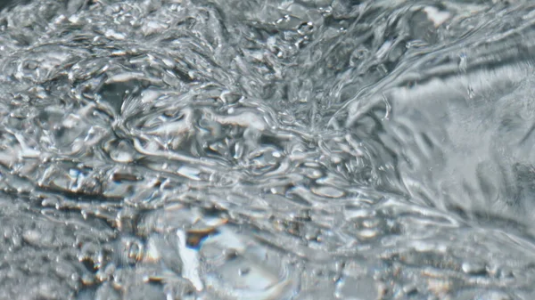 Closeup bubbling aqua texture. Cold water waves moving spinning in fresh beverage in slow motion. Macro cocktail liquid swirling inside glassware top view. Refreshing cool summer drink concept