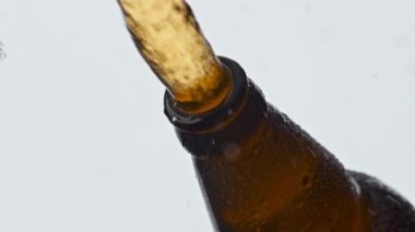 Bira şişesi kapağı yakın plan çekiliyor. Altın karbonatlı bira yavaş çekimde sıçrıyor. Açılış içeceği, beyaz arka plan basıncı altında dökülüyor. Inebriant ipa kapak makrosunun altından kaçar