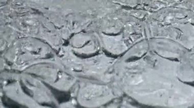 Yakından kaynayan su bardağı. Temiz beyaz arka planda organik sıvı dalgalanma dokusu. Mineral su camları ağır çekimde dönüyor. Tazelik sağlıklı yaşam tarzı konsepti 