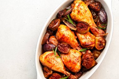 Pişmiş tavuk bacağı, incirli but ve balzamik salamurada kırmızı soğan seramik fırın kabı, beyaz arka plan, üst manzara.