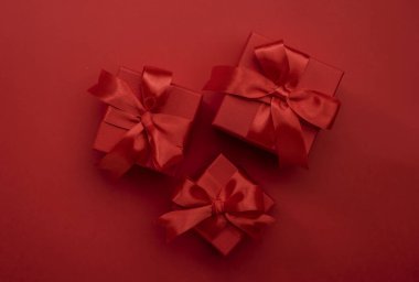 Kırmızı arkaplanda kurdeleli ve fiyonklu kırmızı hediye kutuları. Mutlu Noeller ve mutlu yıllar şablonu. Tatil hazırlığı. Üst Manzara. Boşluk afişini kopyala