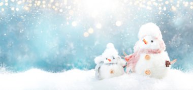 Noel ve yeni yıl kar konsepti şapkalı iki tatlı kardan adam ve mavi arka planda kar yığınları.