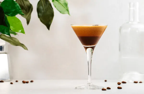 Espresso martini, trendy alcoholic cocktail with vodka, coffee liqueur, syrup and ice, black background, bar tools