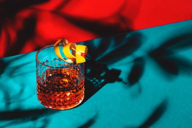 Sazerac, konyak, burbon, absent, acı, şeker ve limon aromalı klasik alkollü kokteyl. Göz kamaştırıcı kırmızı arka plan Sert ışık ve sert gölgeler