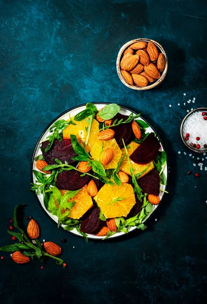 オレンジとビーツサラダ 青いテーブルの背景にアルグラとアーモンド ビーガン健康食品 スペースのコピー — ストック写真