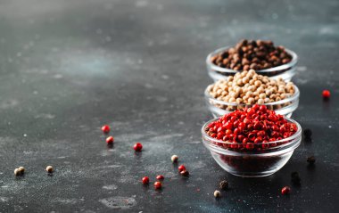 Cam kaselerde siyah, beyaz ve pembe gül biberleri, mutfak masasında çeşitli baharatlar, uzay kopyaları.