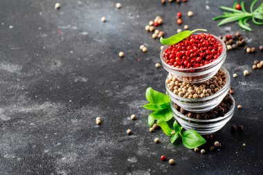 Cam kaselerde siyah, beyaz ve pembe gül biberleri, mutfak masasında çeşitli baharatlar, uzay kopyaları.