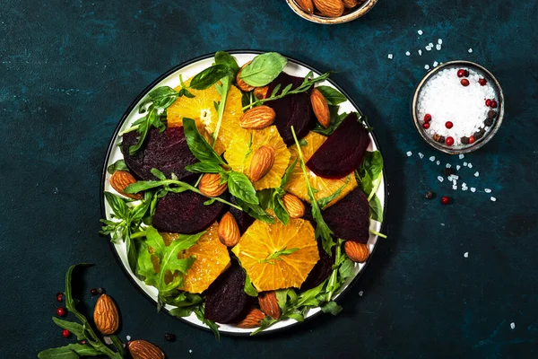 オレンジとビーツサラダ 青いテーブルの背景にアルグラとアーモンド ビーガン健康食品 スペースのコピー — ストック写真