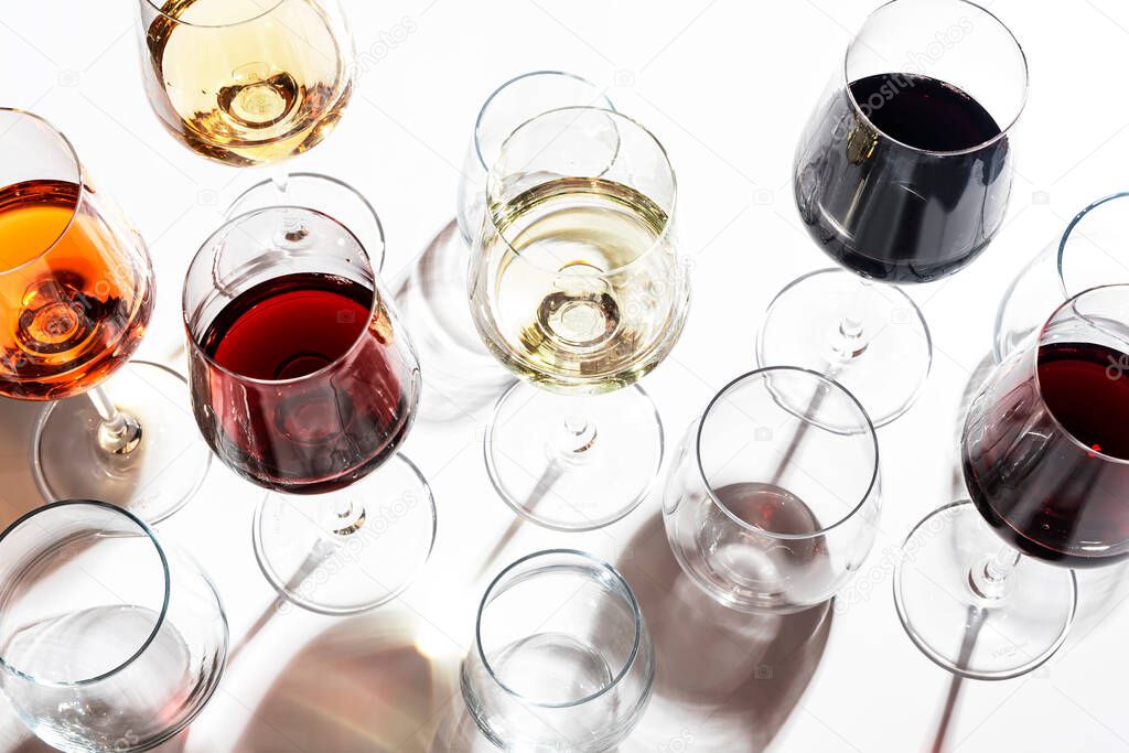 Red, white, rose wines in glasses in assortment on white background, top view. Wine bar, shop, winery, outdoor wine tasting concept. Hard light and harsh shadows
