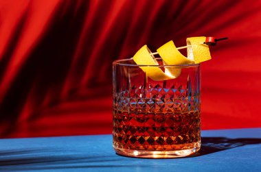 Konyak, burbon, absent, acı, şeker ve limon kabuğuyla Sazerac kokteyli. Göz kamaştırıcı kırmızı arka plan Sert ışık ve sert gölgeler