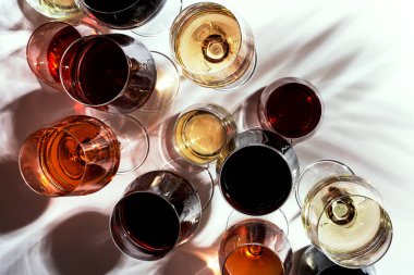 Kırmızı, beyaz, gözlüklü, beyaz arka planda çeşitli gül şarapları, üst manzara. Şarap barı, dükkan, şaraphane, açık hava şarap tatma konsepti. Sert ışık ve sert gölgeler