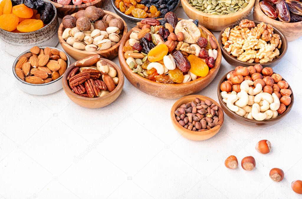 Dried fruits nuts in bowls set. Dry apricots, figs, raisins, walnuts, almonds and other. Healthy nutritious snacks. White table background, top view, copy space